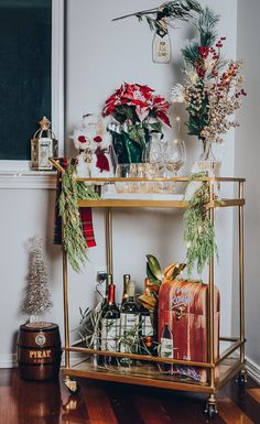 a gold bar cart filled with bottles and flowers on top of a hard wood floor