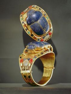 two gold rings with blue and red stones on them, one is in the shape of a turtle