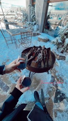 two people toasting wine over an open fire pit in the snow with chairs and tables behind them