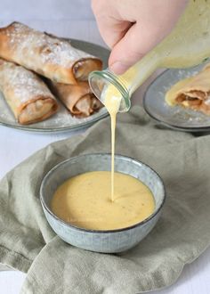 a person pouring sauce into a bowl filled with pastries