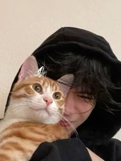 a woman holding an orange and white cat in her arms while wearing a black hoodie