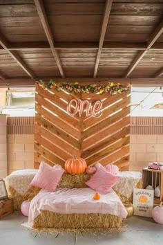 a hay bale bed with pink pillows and pumpkins on it in front of a wooden wall