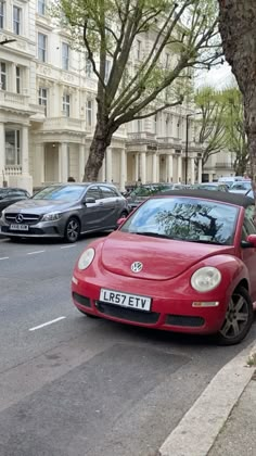 a red car parked on the side of a street next to a tree and buildings