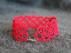 red crocheted lace bracelet with gold chains on grey carpeted surface, closeup