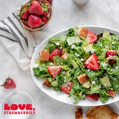 a salad with strawberries and avocado in a bowl next to toasted bread