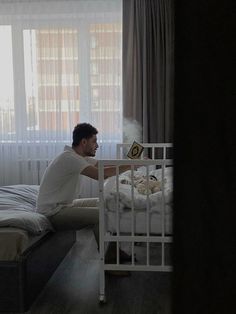 a man sitting on top of a bed next to a baby crib