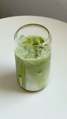 a glass filled with green liquid sitting on top of a white table next to a banana