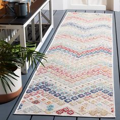 a white rug with multicolored designs on the floor next to a potted plant