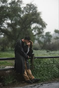 a man and woman sitting on a bench in the rain kissing each other with an umbrella over their heads