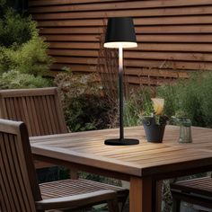 a table with a lamp on it and some chairs around it in front of a wooden wall