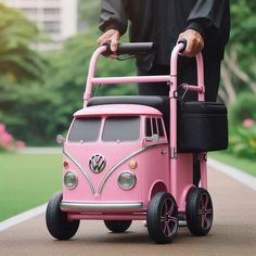 a man pushing a pink toy bus down a road with his hand on the handlebars