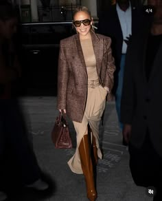 a woman walking down the street wearing brown boots and a blazer with an overcoat