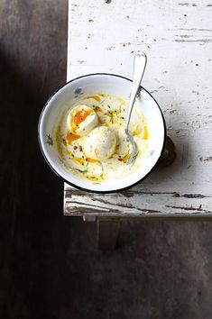 a white bowl filled with food sitting on top of a wooden table next to a fork