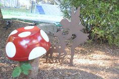 a red mushroom sitting on top of a tree stump next to a metal sign that says fairy land