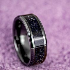 black ceramic ring with blue glitter inlays on purple carpeted surface, close up