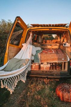 the back end of an orange van with hammocks and blankets on it's bed