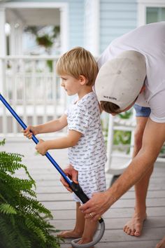 a man helping a little boy with his gardening tools on the deck outside their house