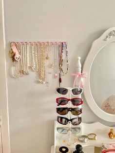 a white vanity topped with lots of jewelry and sunglasses next to a mirror on the wall