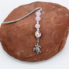 a pink beaded bracelet with a silver turtle charm on top of it and a chain attached to the clasp