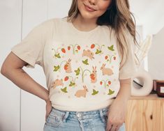 This cute cottagecore shirt features sweet strawberries and bunnies. This trendy design will your new favorite shirt that you reach for again and again. Makes a great gift for any rabbit lover. * Q U I C K * F A C T S * ♥ Solid colors are 100% cotton ♥ Heather colors are cotton/poly blend ♥ Design is high quality digital print ♥ Wash and dry normally (on cool for best results) * S I Z I N G * ♥ Models are wearing size small ♥ Sizing is unisex so runs like men's, though not overly large ♥ Most wo Cute Strawberry Print Shirt, Cute Summer Tops With Bunny Design, Cute Bunny Print Tops For Spring, Cute Bunny Design Summer Tops, Cute Summer Top With Bunny Design, Cute Cotton Tops With Bunny Design, Cute Cotton Top With Bunny Design, Spring Crew Neck Tops With Bunny Design, Spring Bunny Design Short Sleeve Top