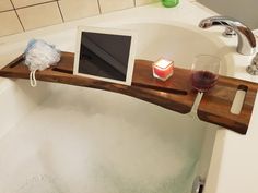 a bath tub with a wooden shelf holding a tablet and two glasses of wine next to it