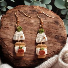 a pair of earrings is sitting on a piece of wood next to some plants and leaves