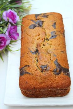 a loaf of cake sitting on top of a white plate next to purple and pink flowers