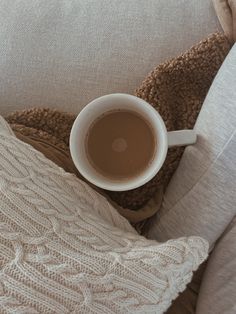 a cup of coffee sitting on top of a white couch next to a brown blanket