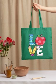 a person holding up a green bag with the word love on it and an apple