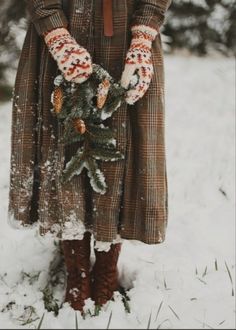 a woman standing in the snow with her hands on a small christmas tree and wearing gloves