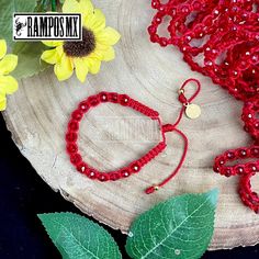 a red beaded bracelet and matching necklace on a wooden plate with flowers in the background