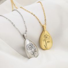 two pendants with flowers on them are sitting on a white cloth, one is gold and the other is silver