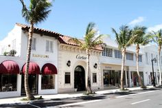 palm trees line the street in front of a white building with red awnings