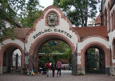 two people walking under an entrance to a zoo