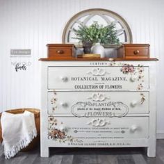 a white dresser with flowers on it and a potted plant sitting on top of it