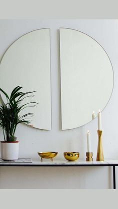 two mirrors are on the wall above a table with candles and a potted plant