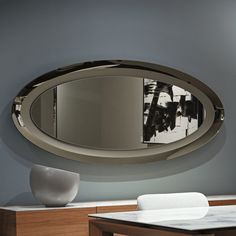 a round mirror is hanging on the wall above a table with a vase in front of it