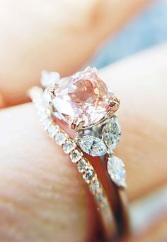 a woman's hand holding a ring with a pink diamond in the center and two white diamonds on each band