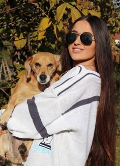 a woman with sunglasses holding a dog in her arms and looking at the camera while standing outside