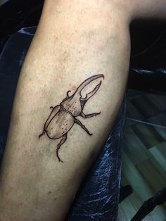 a beetle tattoo on the leg of a person's arm, it is black and brown