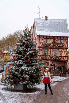 a woman standing next to a christmas tree in front of a red and brown building