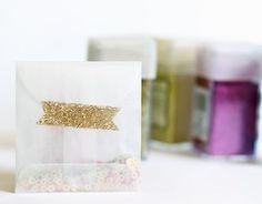 two bags with gold glitter on them sitting next to some other crafting supplies in the background