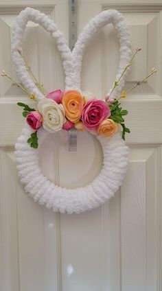 a white wreath with pink and orange flowers hanging on the front door to make an easter bunny decoration