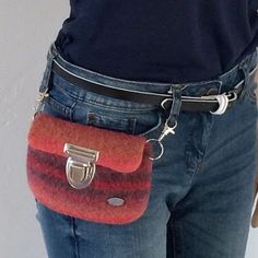 a woman is holding a red and black purse in her hand while wearing blue jeans