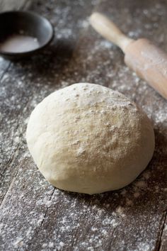 a ball of bread sitting on top of a wooden table next to a rolling pin