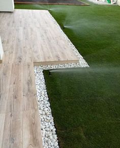 a wooden walkway with grass and rocks on the ground in front of a white house