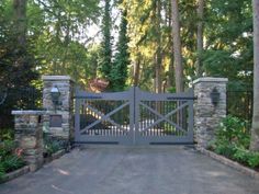 a gated driveway with stone pillars leading into the woods