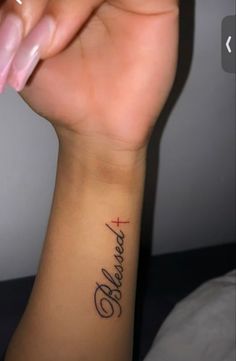 a woman's wrist tattoo with the words believe and a cross in cursive writing