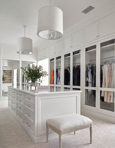 a large white closet with lots of clothes hanging on the wall and a bench in front of it