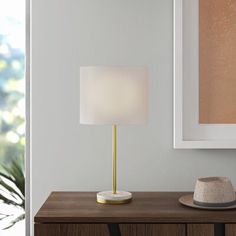 a hat on a table next to a lamp in a room with white walls and wooden furniture